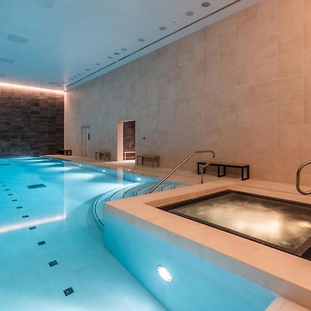 Citysuites 2 Aparthotel Manchester Bagian luar foto The photo shows an indoor swimming pool area. The pool is a bright blue color and features smooth, tiled surfaces. On one side, there is a hot tub area with steps leading into it. The walls are made of light-colored stone, and there is ambient lighti
