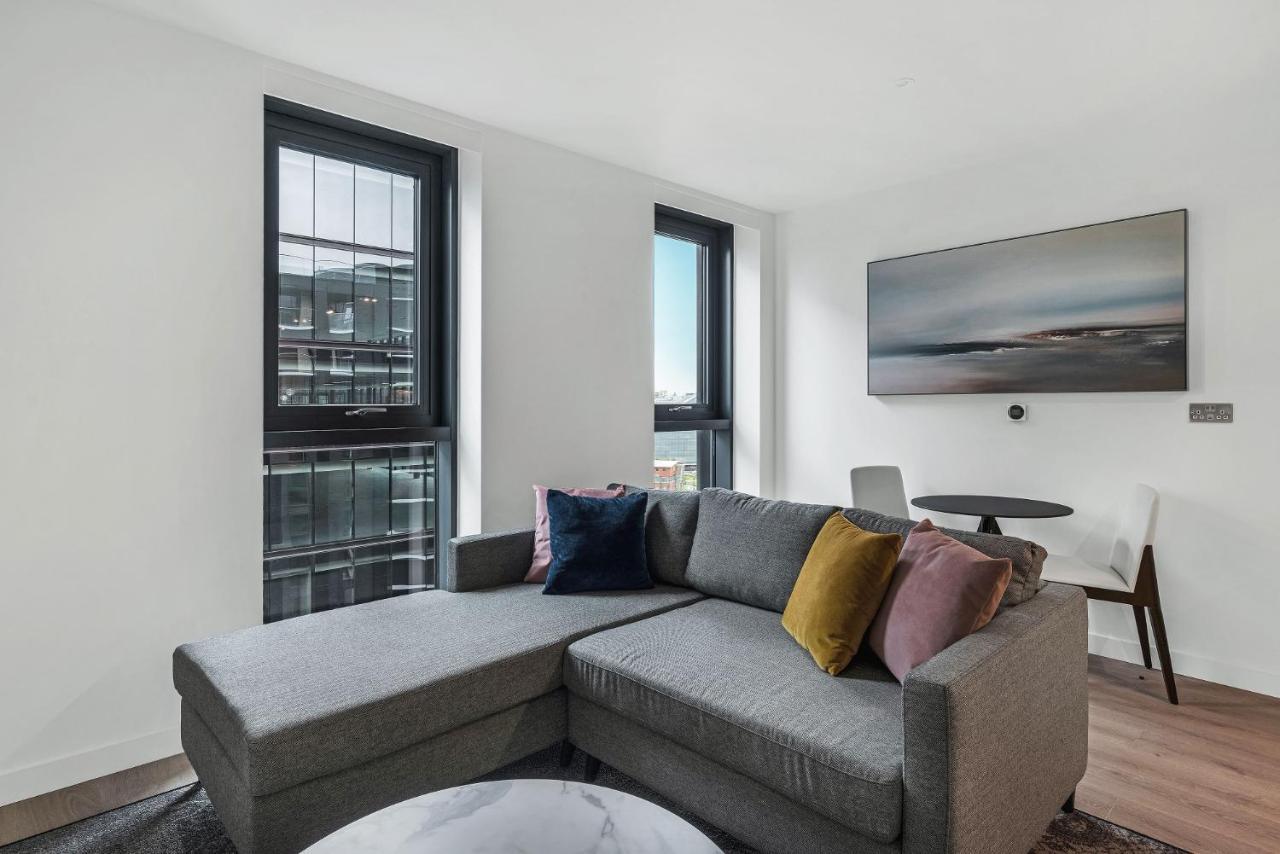 Citysuites 2 Aparthotel Manchester Bagian luar foto The photo shows a modern living space featuring a gray sectional sofa adorned with colorful throw pillows. There are large windows allowing natural light to fill the room, offering a view of the outdoors. A wall-mounted television is positioned above
