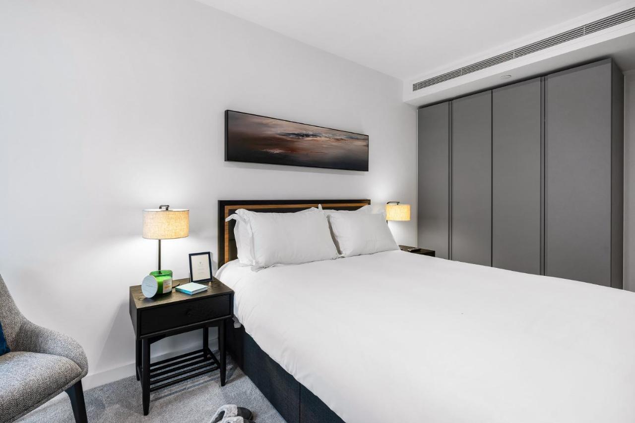 Citysuites 2 Aparthotel Manchester Bagian luar foto The photo shows a modern bedroom with a neatly made bed featuring white linens and pillows. Flanking the bed are two bedside tables, each with a lamp providing soft lighting. There is a piece of artwork above the bed, which appears to depict a landsc