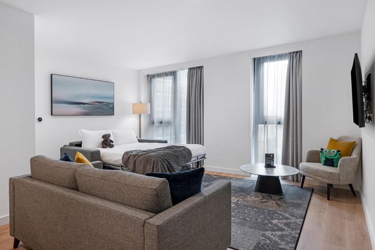 Citysuites 2 Aparthotel Manchester Bagian luar foto The photo shows a modern living space that incorporates a cozy and inviting atmosphere. It features a light-colored couch with colorful cushions, positioned in front of a coffee table. There's a comfortable armchair nearby, and a throw blanket is dra