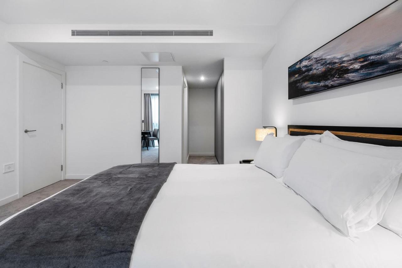 Citysuites 2 Aparthotel Manchester Bagian luar foto The photo shows a modern bedroom with a minimalistic design. In the foreground, there is a neatly made bed with white linens and a dark gray throw blanket. To the side, there is a bedside lamp and a piece of abstract artwork on the wall above the bed