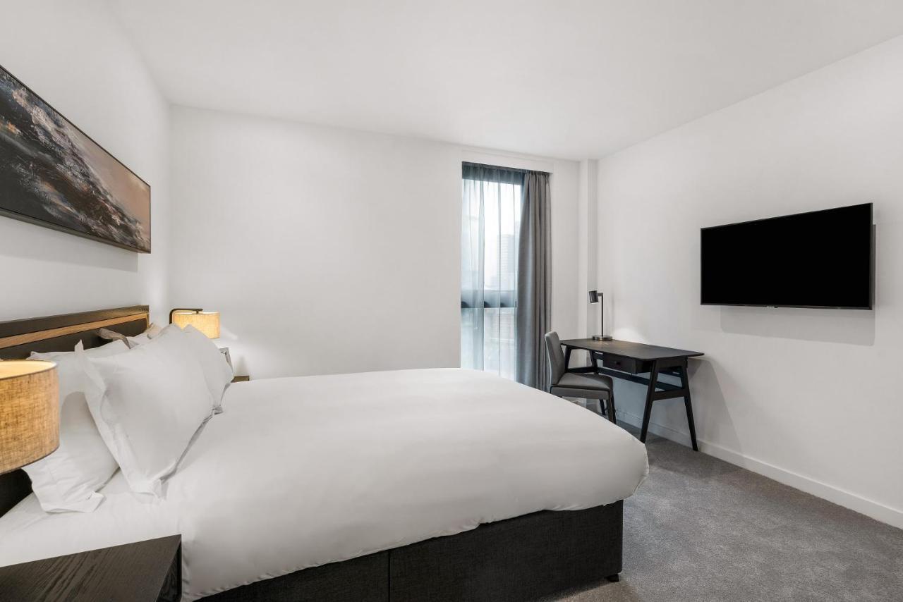 Citysuites 2 Aparthotel Manchester Bagian luar foto The photo shows a modern hotel room featuring a large bed with white linens and a dark headboard. There are two bedside lamps on either side of the bed. A desk with a chair is placed against one wall, and a flat-screen TV is mounted on another wall. 