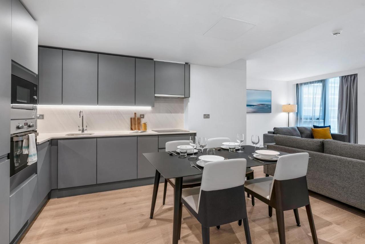Citysuites 2 Aparthotel Manchester Bagian luar foto The photo shows a modern, open-concept kitchen and living area. The kitchen features sleek, gray cabinetry with a countertop, a sink, and built-in appliances. There are cooking utensils displayed on the countertop. Next to the kitchen, there is a din