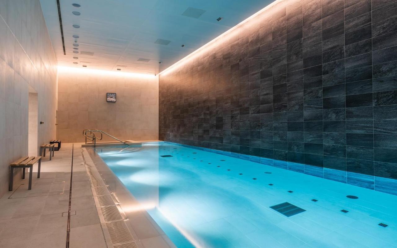 Citysuites 2 Aparthotel Manchester Bagian luar foto The photo shows an indoor swimming pool area. The pool is illuminated with a soft blue light, creating a calming atmosphere. The walls are designed with dark tiles, and there is a lighter tiled area surrounding the pool. Ambient lighting is installed