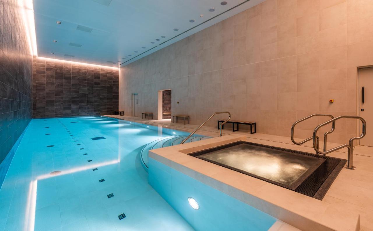 Citysuites 2 Aparthotel Manchester Bagian luar foto The photo shows an indoor swimming pool area. The pool is a bright blue color and features smooth, tiled surfaces. On one side, there is a hot tub area with steps leading into it. The walls are made of light-colored stone, and there is ambient lighti