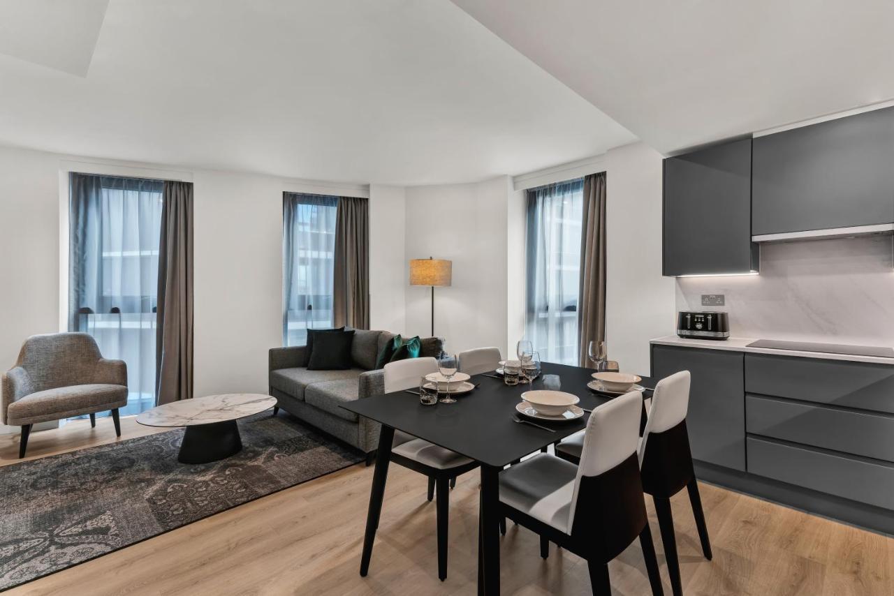 Citysuites 2 Aparthotel Manchester Bagian luar foto The photo shows a modern living space that includes a dining area and a seating area. There's a sleek black dining table set with plates and cutlery, accompanied by white and black chairs. To one side, a comfortable gray sofa faces the dining area, c