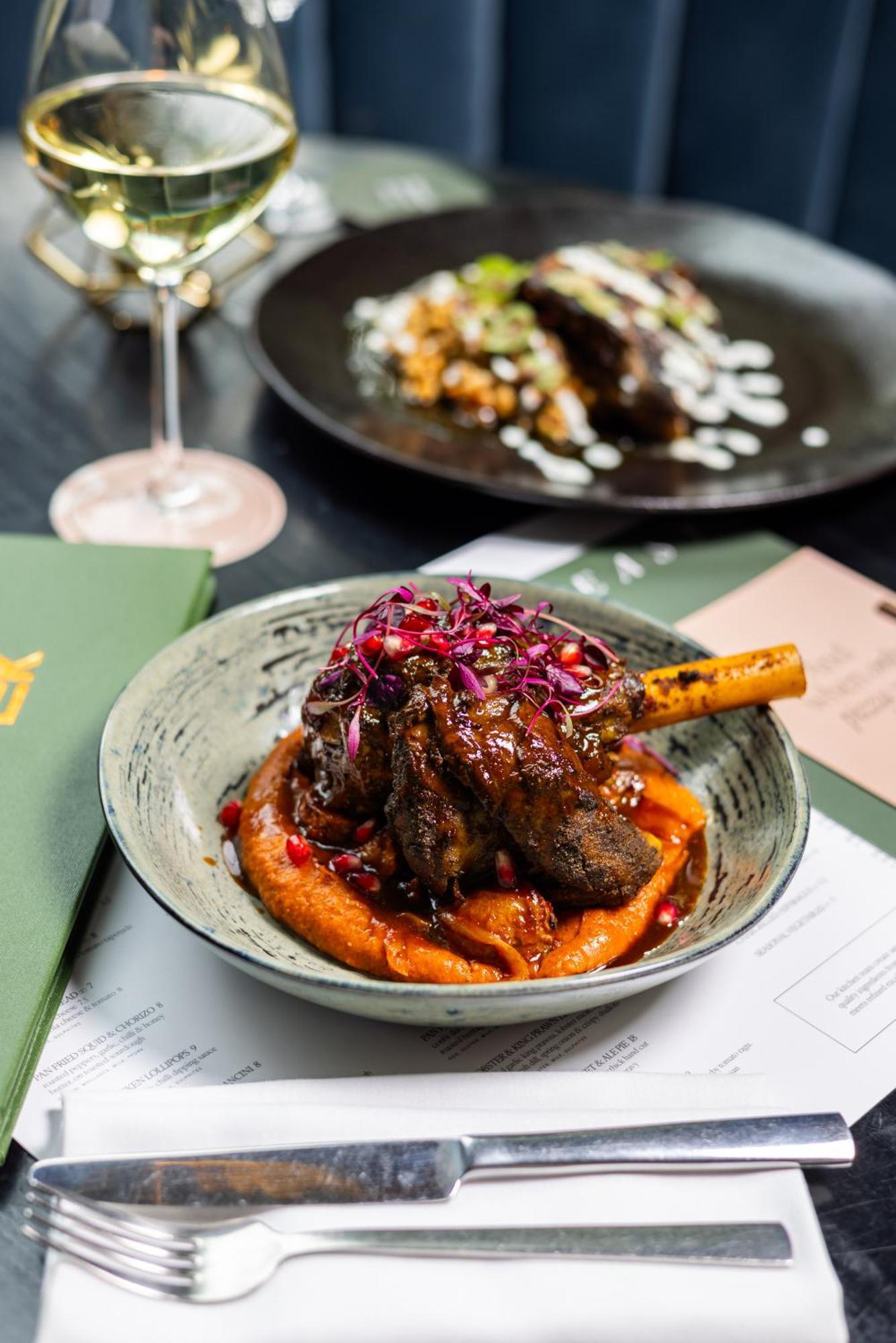 Citysuites 2 Aparthotel Manchester Bagian luar foto The photo showcases a beautifully presented dish featuring a piece of slow-cooked meat with a bone, likely lamb, sitting atop a vibrant orange puree. The meat is glazed with a rich sauce and garnished with small pieces of red pomegranate and purple m