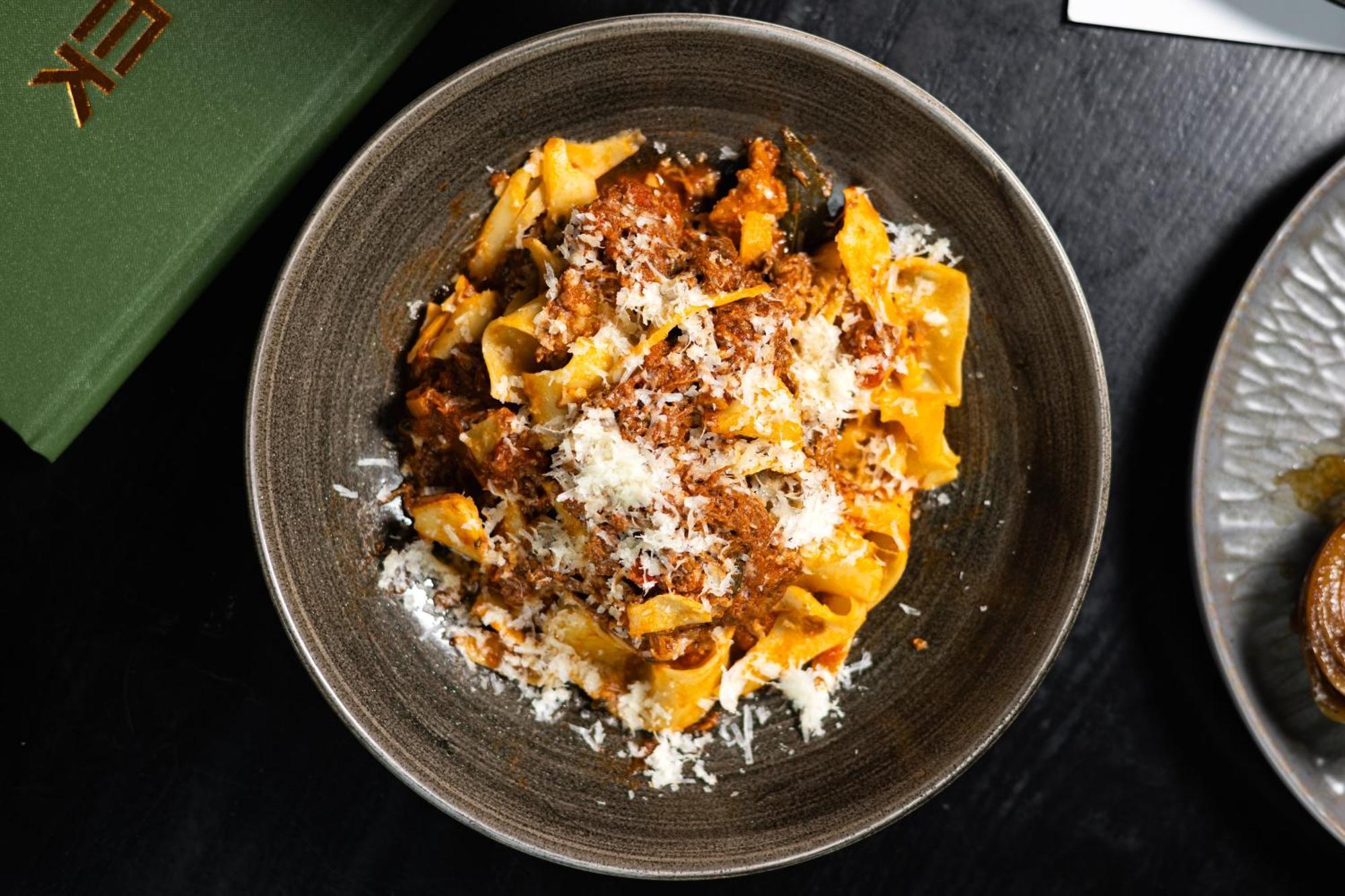 Citysuites 2 Aparthotel Manchester Bagian luar foto The photo shows a bowl of pasta featuring wide, ribbon-like noodles, likely pappardelle, fully coated in a rich meat sauce. The dish is garnished with a generous sprinkling of grated cheese, adding a creamy texture to the presentation. The dark bowl 